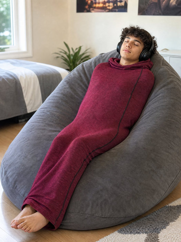 Teen relaxing on a beanbag in the red Snuggl Pod with headphones on